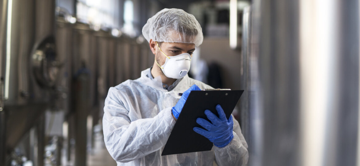 Technologist in white uniform checking quality in industrial production factory.